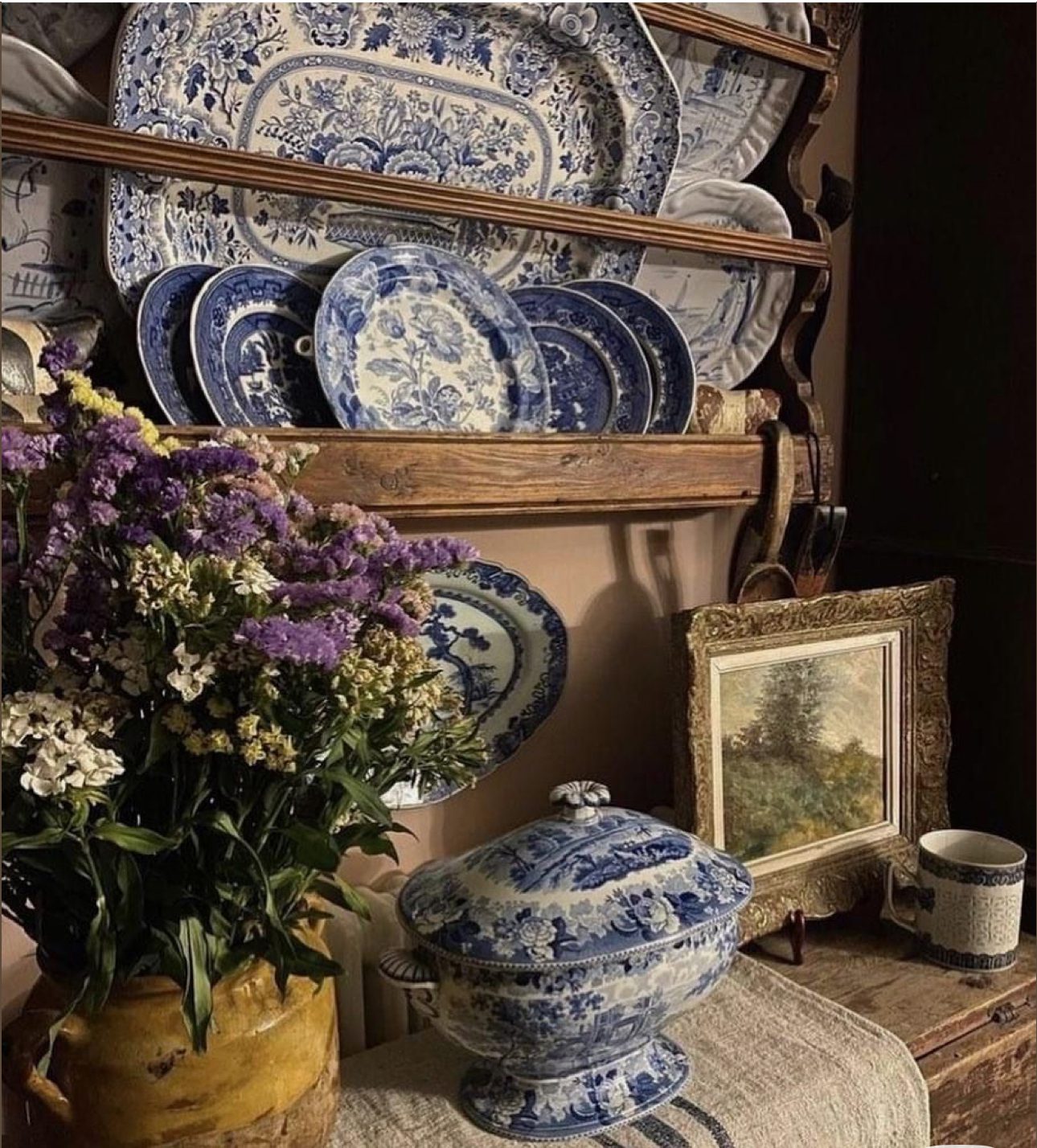 A rustic shelf with blue and white china, flowers, and antique decor.