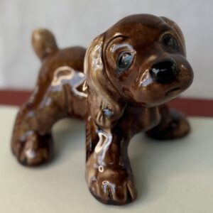 A small, shiny brown ceramic puppy figurine with big eyes.