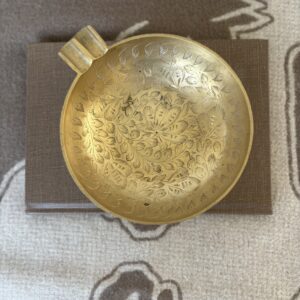 Antique brass cup with intricate engravings on a brown cloth.