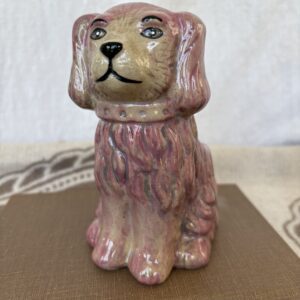 A small ceramic dog figurine with a pinkish hue and detailed fur.