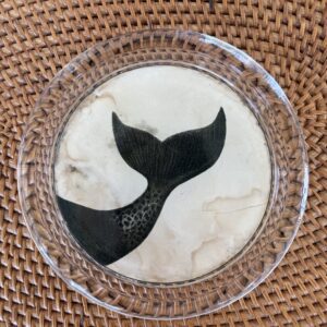 A black whale tail silhouette on a round white ceramic plate.