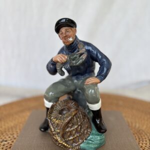 Figurine of a fisherman holding a fish beside a fishing net.