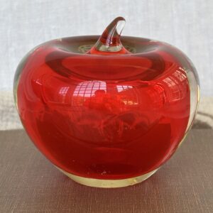 A shiny red glass apple decoration on a wooden surface.