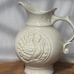 Ornate cream-colored ceramic pitcher with embossed floral design.
