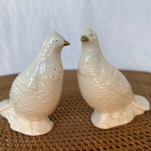 Two white ceramic bird figurines on a woven surface.